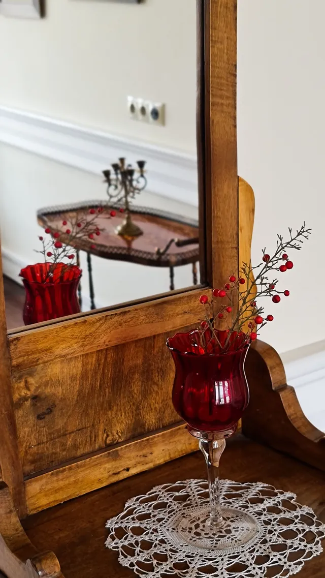 Close-up of a wood-framed dressing mirror with a red glass candle holder on a lace doily